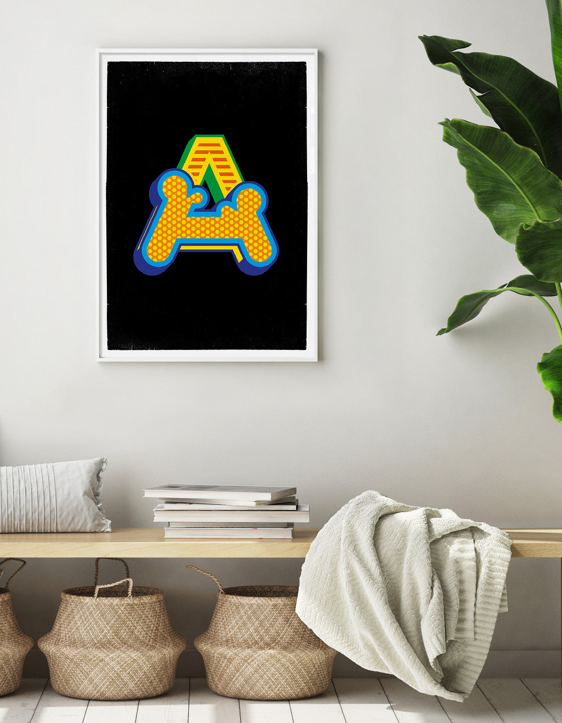 Lifestyle image of A initial circus print on a black background against a neutral wall with bench and seagrass baskets, blankets and books are resting on the bench and a greeen plant is just in shot