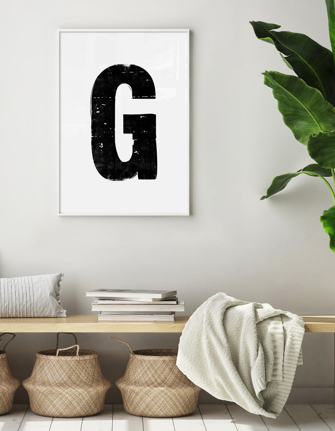 lifestyle image showing the letter G monochrome alphabet print on the wall above a bench seat with a pile of books and woven baskets underneath