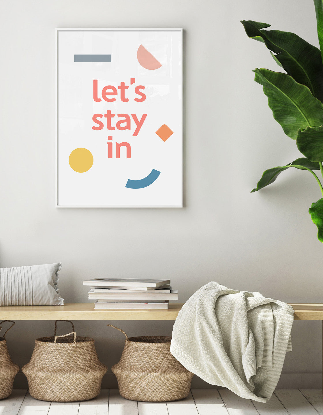 Let's stay in typography print shown on the wall above a bench with storage baskets a blanket and a palm plant