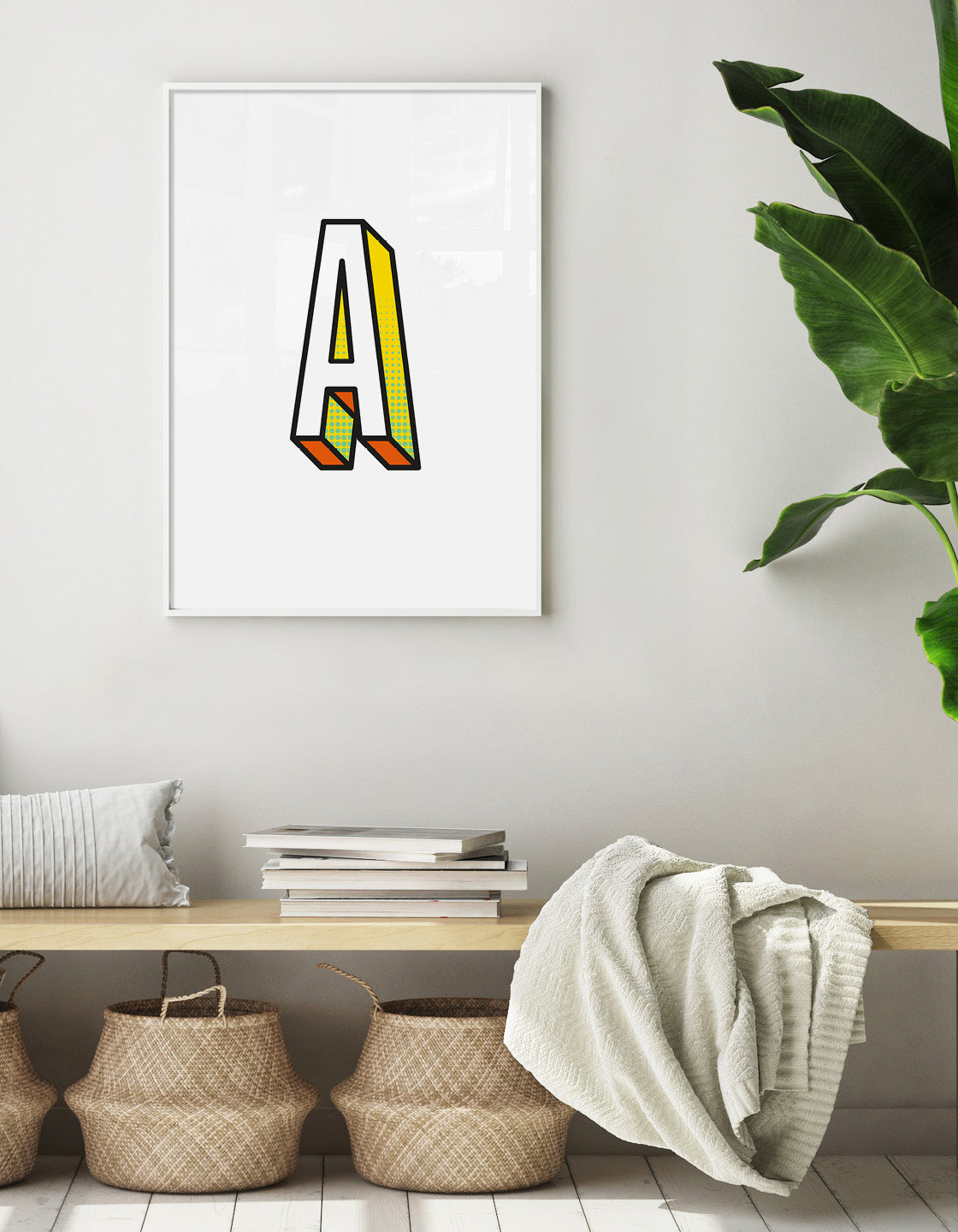 Letter A initial 3D print shown on a neutral colour wall with a wooden bench with seagrass baskets underneath, blankets and books on top and a green plants off to one side